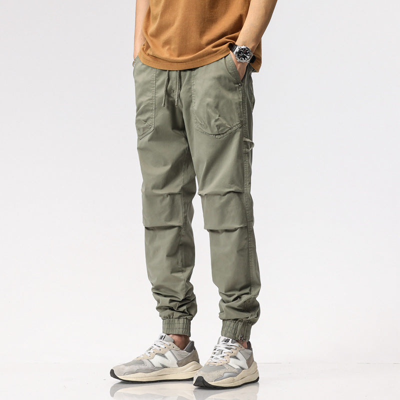 Pantaloni cargo uomo verde oliva, stile casual, con tasche multiple e polsini elasticizzati, abbinati a scarpe sportive grigie e maglietta marrone.