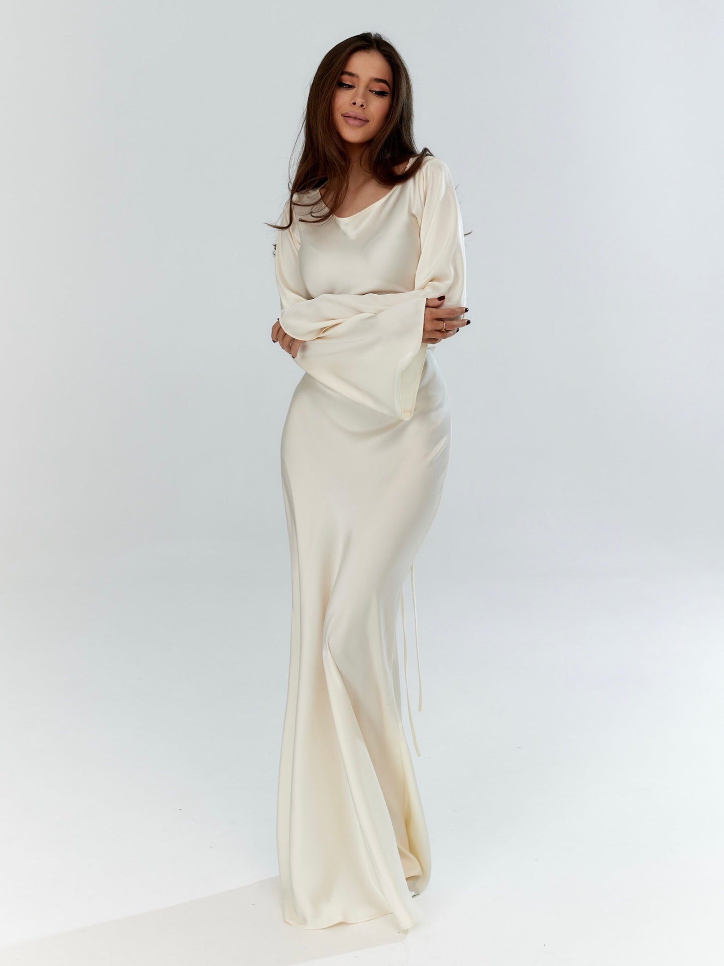 Donna in abito da sera bianco elegante, maniche lunghe, posa su sfondo bianco. Moda femminile, abbigliamento elegante, stile sofisticato.