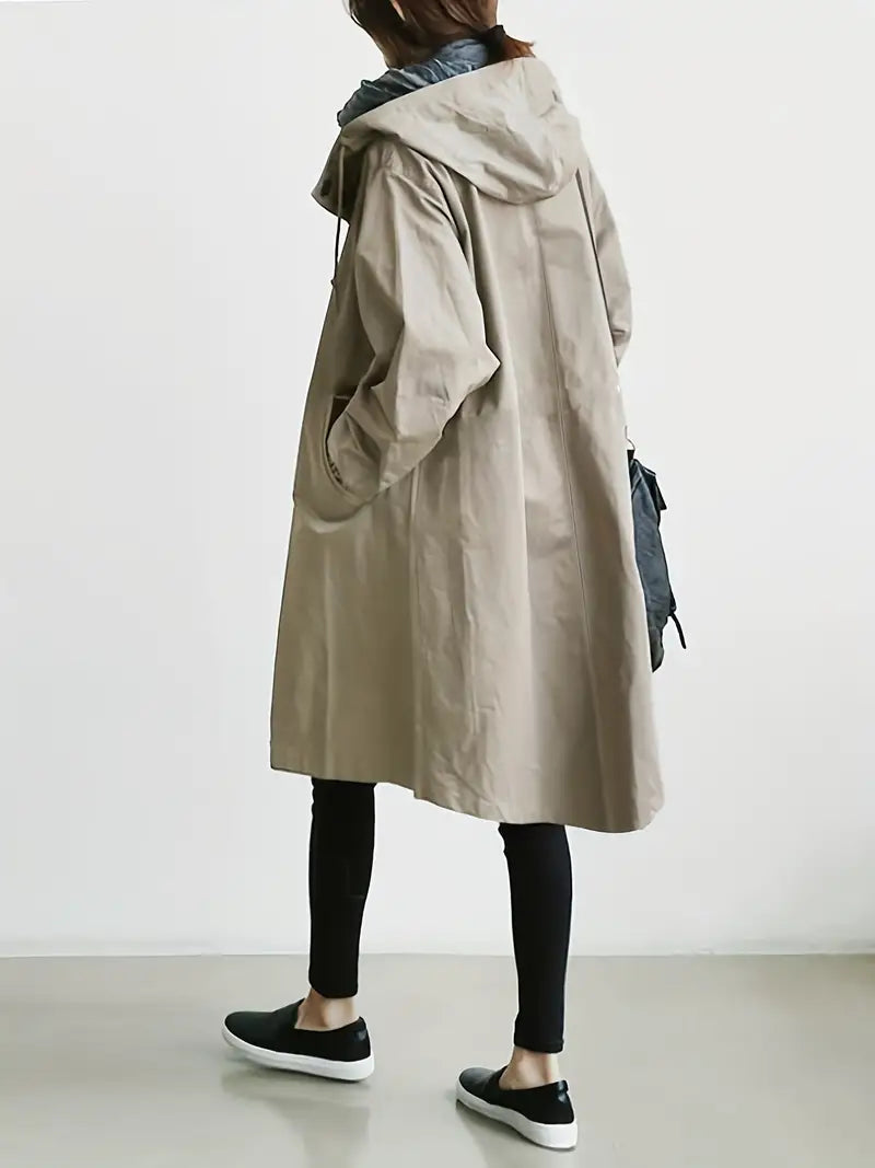 Donna con cappotto beige oversize, cappuccio, leggings neri e scarpe da ginnastica nere. Moda autunnale casual, stile urbano minimalista.