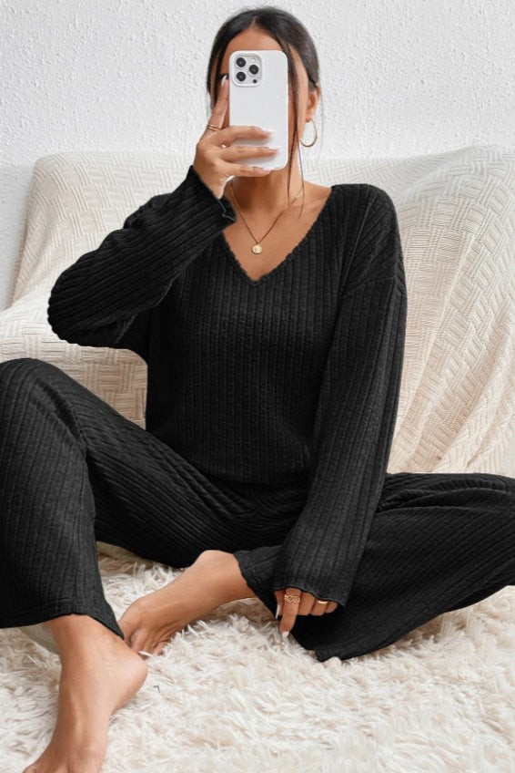 Donna seduta su tappeto bianco, indossa pigiama nero a coste, scatta selfie con smartphone. Look casual e confortevole, moda loungewear.