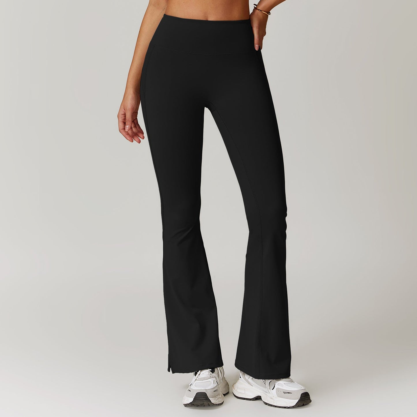 Pantaloni yoga neri a zampa, vita alta, indossati da una donna. Perfetti per fitness e moda casual. Scarpe da ginnastica bianche abbinate.