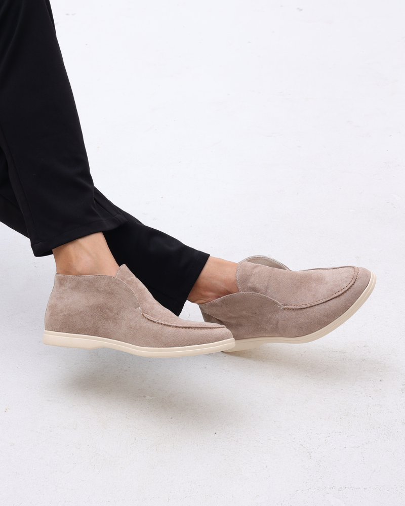 Scarpe mocassino beige in pelle scamosciata, indossate con pantaloni neri. Design elegante e casual, perfette per look quotidiani e formali.