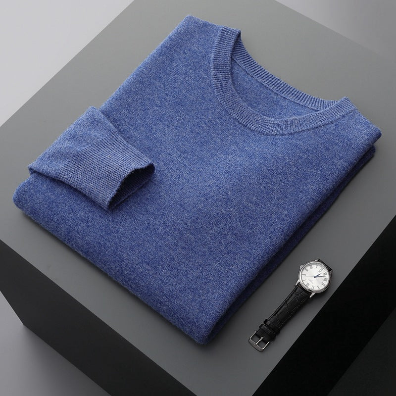 Maglione blu in cashmere piegato su tavolo grigio, accanto a orologio da polso elegante con cinturino in pelle nera e quadrante bianco.