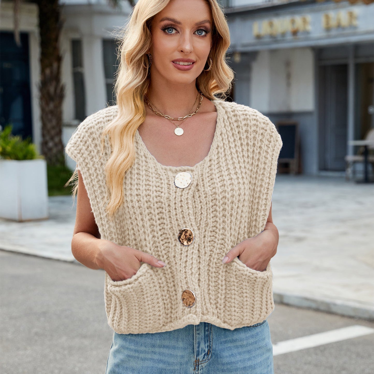 Donna con gilet lavorato a maglia beige, bottoni grandi, posa all'aperto. Moda autunnale, abbigliamento casual, stile urbano.