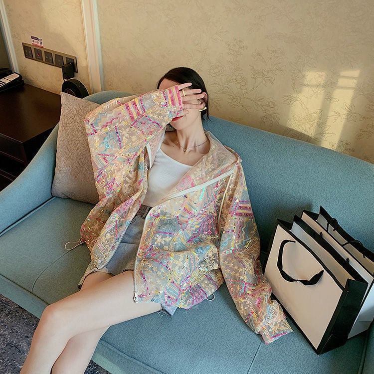 Donna seduta su divano blu indossa giacca colorata e copre il viso con la mano; accanto a lei, borse shopping bianche. Moda casual, relax.
