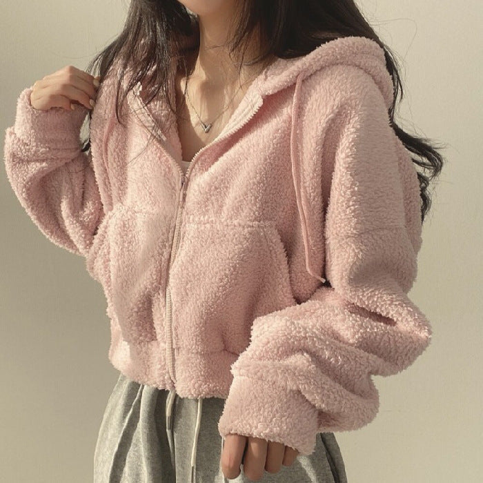 Donna con felpa rosa in pile, cappuccio e zip, indossa pantaloni grigi. Moda casual autunnale, abbigliamento comodo e caldo.