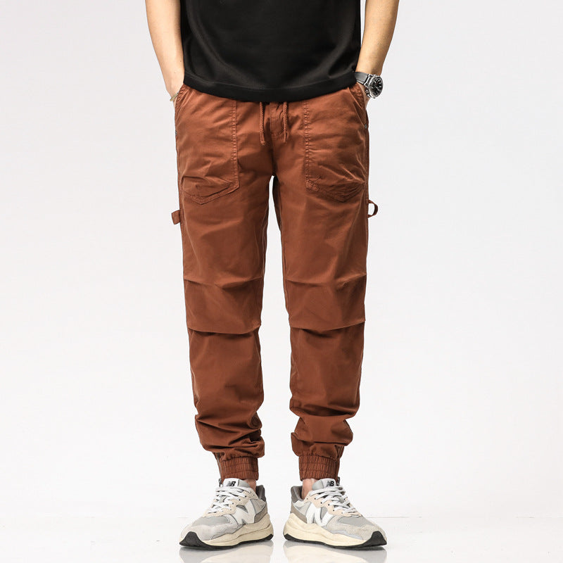 Pantaloni cargo marroni da uomo, tasche multiple, stile casual, abbinati a scarpe sportive bianche e nere, moda maschile contemporanea.