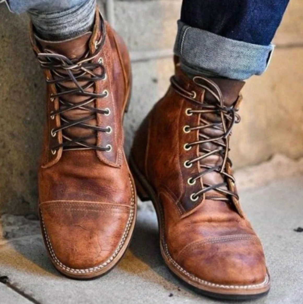 Stivali in pelle marrone da uomo, stile vintage, con lacci e cuciture a vista, indossati con jeans arrotolati. Scarpe moda autunno inverno.
