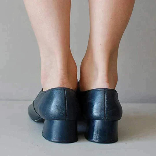 Scarpe nere con tacco basso indossate da una persona, viste da dietro. Calzature eleganti in pelle, ideali per look formali e casual.