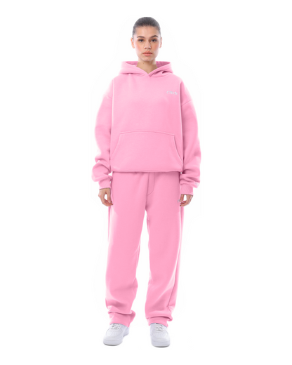 Donna in tuta rosa, felpa con cappuccio e pantaloni abbinati, scarpe bianche. Moda casual, abbigliamento sportivo, stile confortevole.