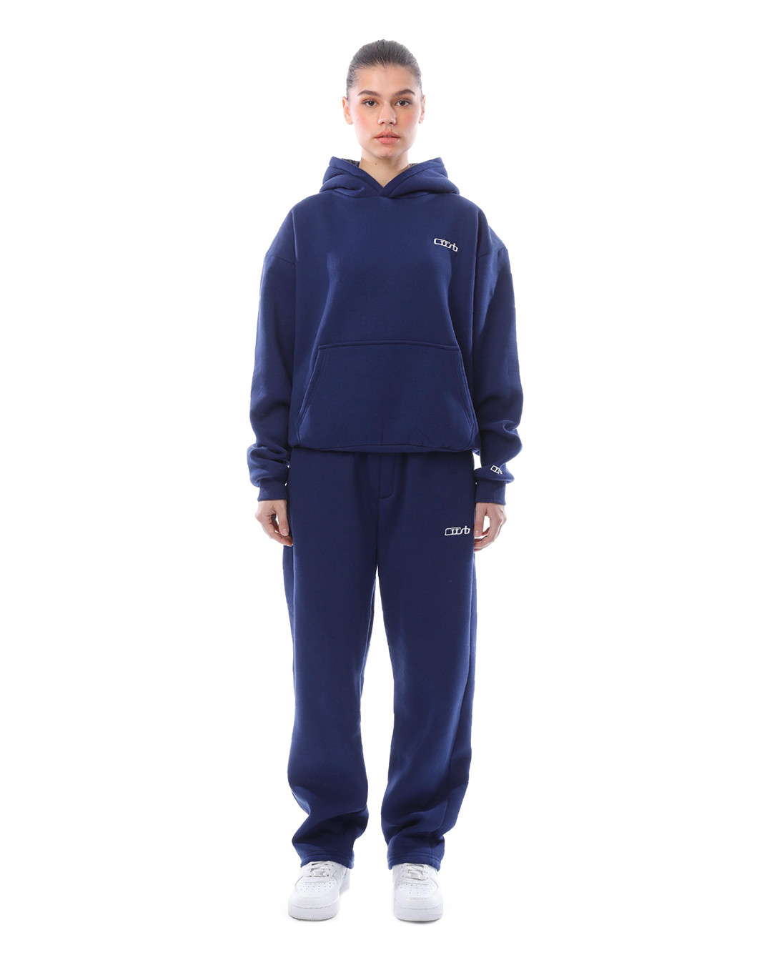 Donna in tuta sportiva blu scuro, felpa con cappuccio e pantaloni abbinati, scarpe bianche. Abbigliamento casual, moda streetwear.