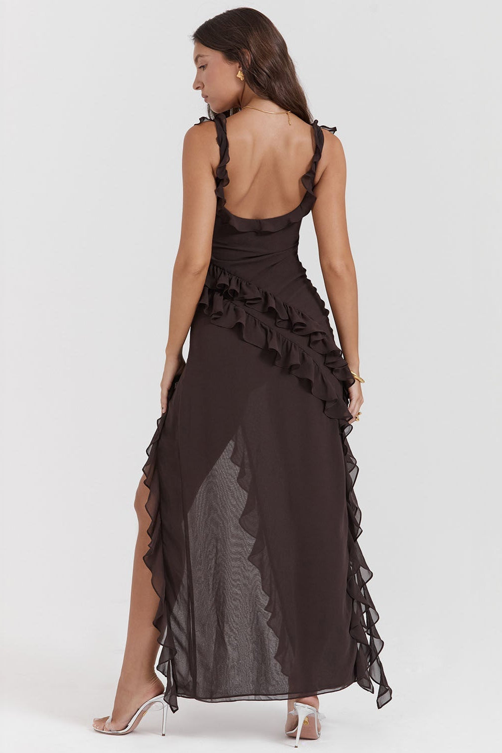 Donna in abito lungo nero con volant, schiena scoperta e spacco laterale, indossa tacchi alti. Moda elegante, abbigliamento da sera femminile.