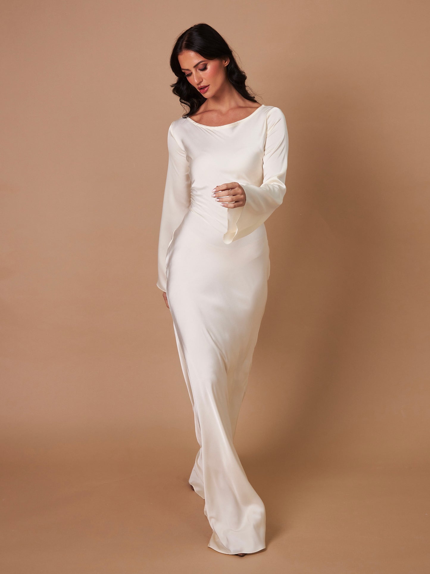 Donna in abito da sposa bianco elegante, maniche lunghe, su sfondo beige. Moda nuziale, abito da cerimonia, stile classico.