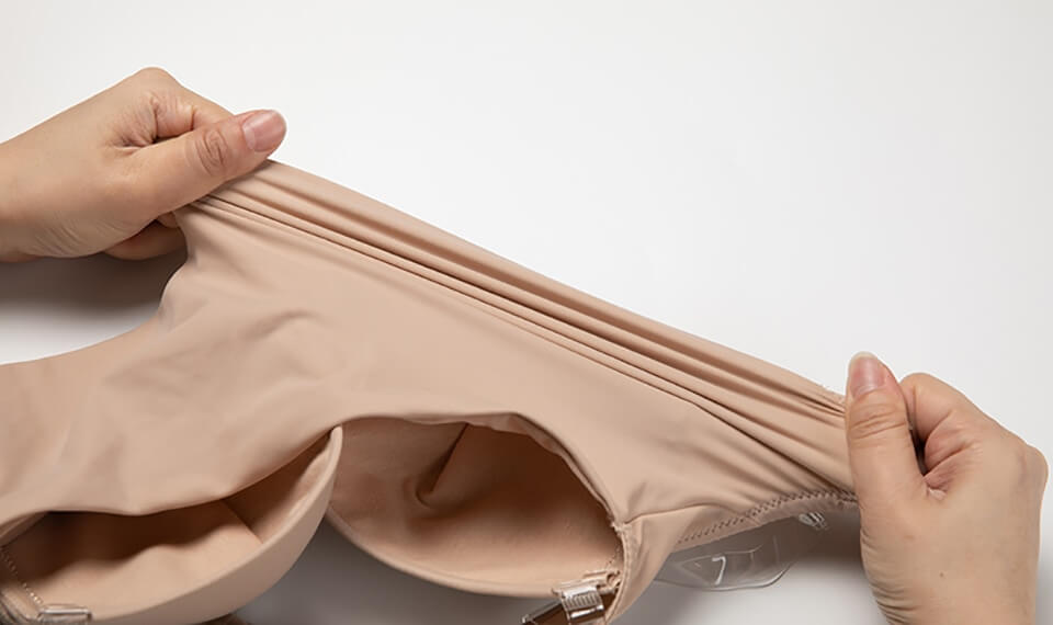 Mani che allungano un reggiseno color carne su sfondo bianco. Tessuto elastico, intimo femminile, comfort, moda donna, lingerie.