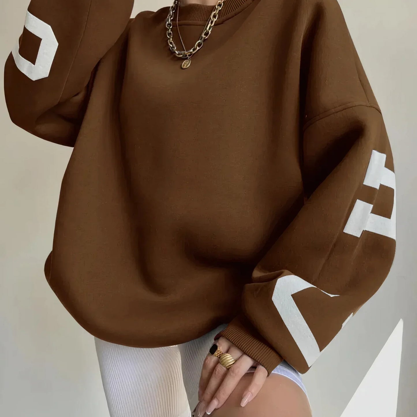 Felpa oversize marrone con stampa bianca sulle maniche, abbinata a pantaloncini bianchi a coste. Look casual e moderno, moda streetwear.