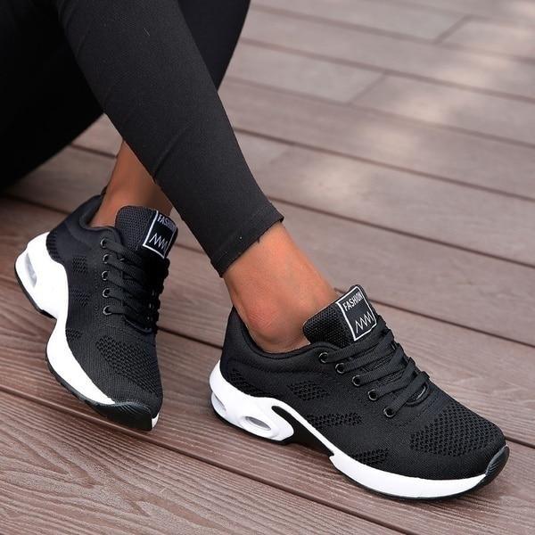 Scarpe da ginnastica nere su pavimento in legno, design moderno e traspirante, ideali per sport e tempo libero. Scarpe sportive donna eleganti.