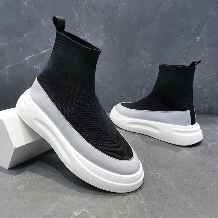 Scarpe da ginnastica nere e bianche con suola spessa, design moderno e calzino elastico, su sfondo grigio. Sneakers alla moda, tendenza 2023.