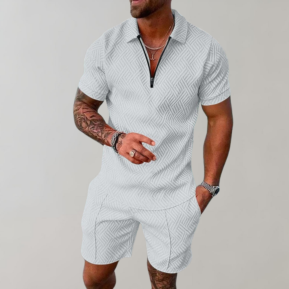 Uomo con tuta estiva bianca a maniche corte, motivo geometrico, collana e orologio. Moda maschile casual, abbigliamento estivo elegante.