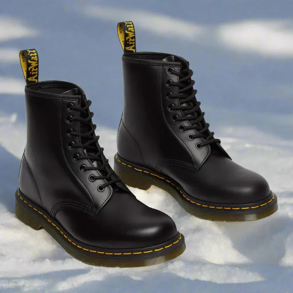 Stivali Dr. Martens neri su neve, classico design in pelle con cuciture gialle, suola robusta. Scarpe iconiche, moda invernale, calzature resistenti.