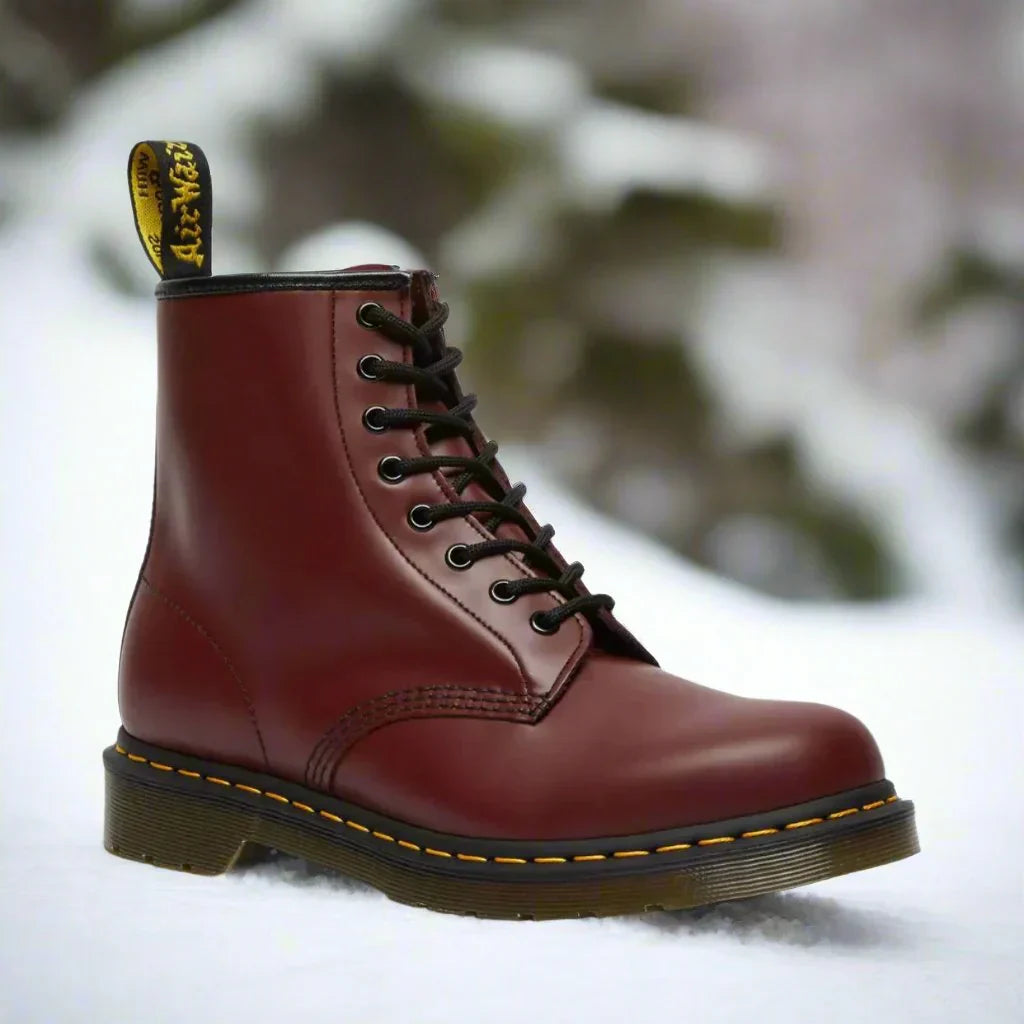 Stivale Dr. Martens rosso ciliegia su sfondo innevato, con cuciture gialle e suola robusta. Calzature iconiche, moda invernale, stile punk.