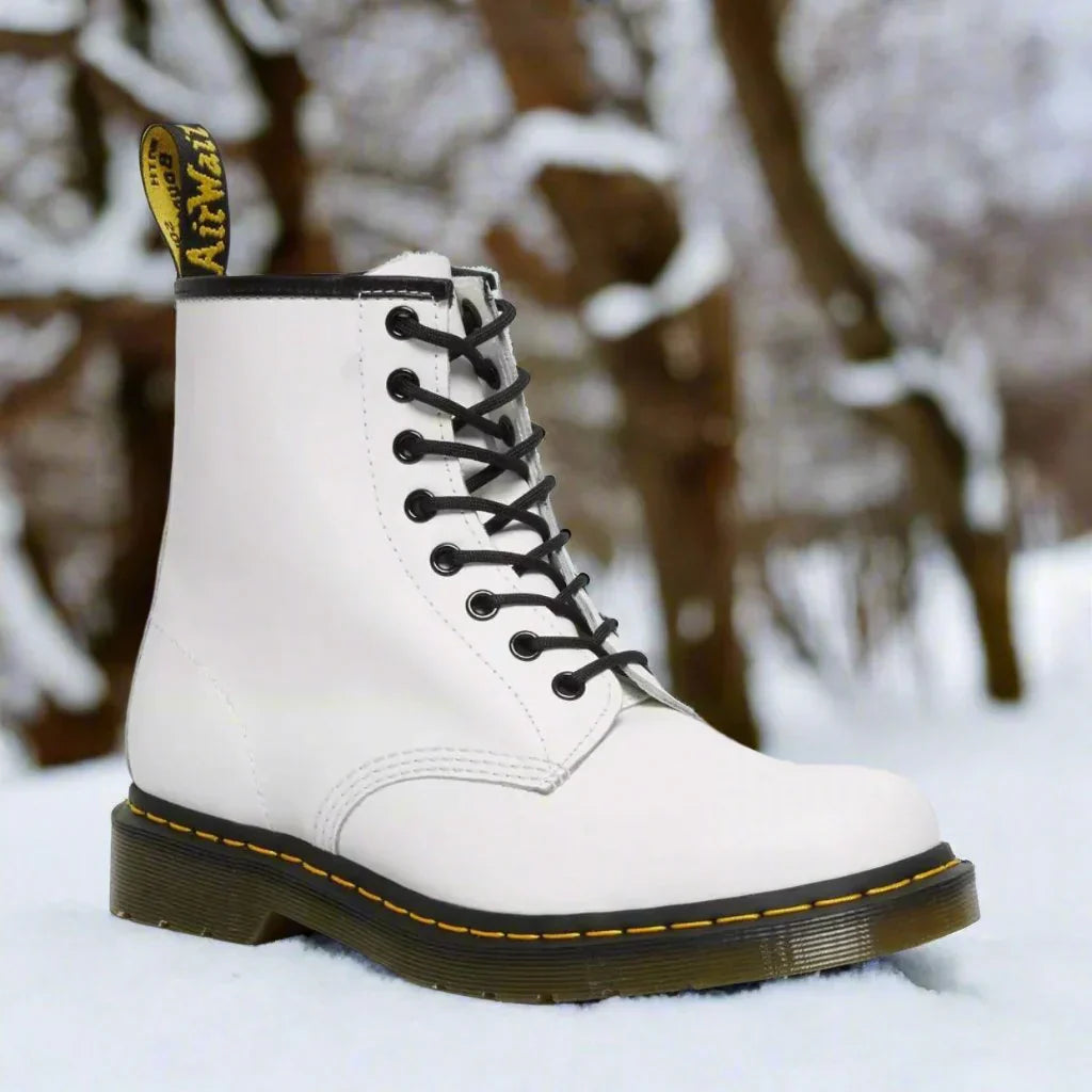 Stivale Dr. Martens bianco su sfondo innevato, design iconico con cuciture gialle e suola robusta. Calzature invernali moda.