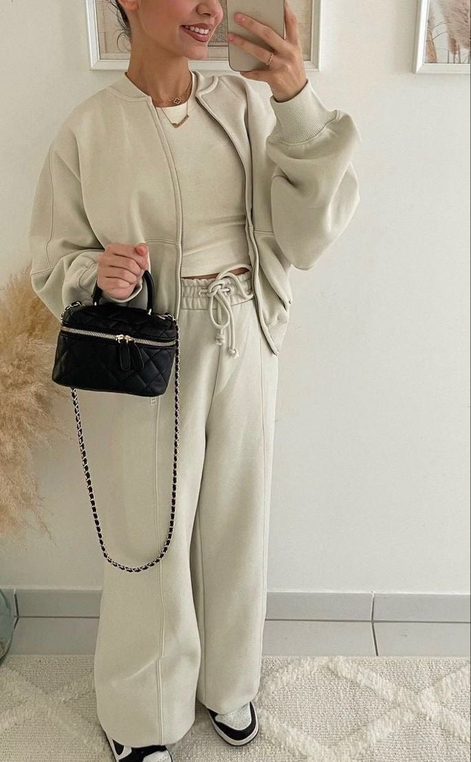 Donna in abbigliamento casual beige con borsa nera trapuntata, pantaloni larghi e sneakers. Moda autunnale, stile comodo ed elegante.