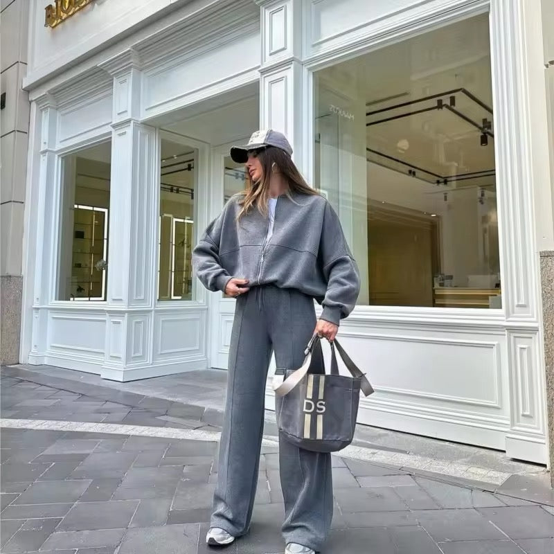 Donna con abbigliamento sportivo grigio, cappellino e borsa DS davanti a negozio elegante. Moda casual, street style, tendenze autunno.