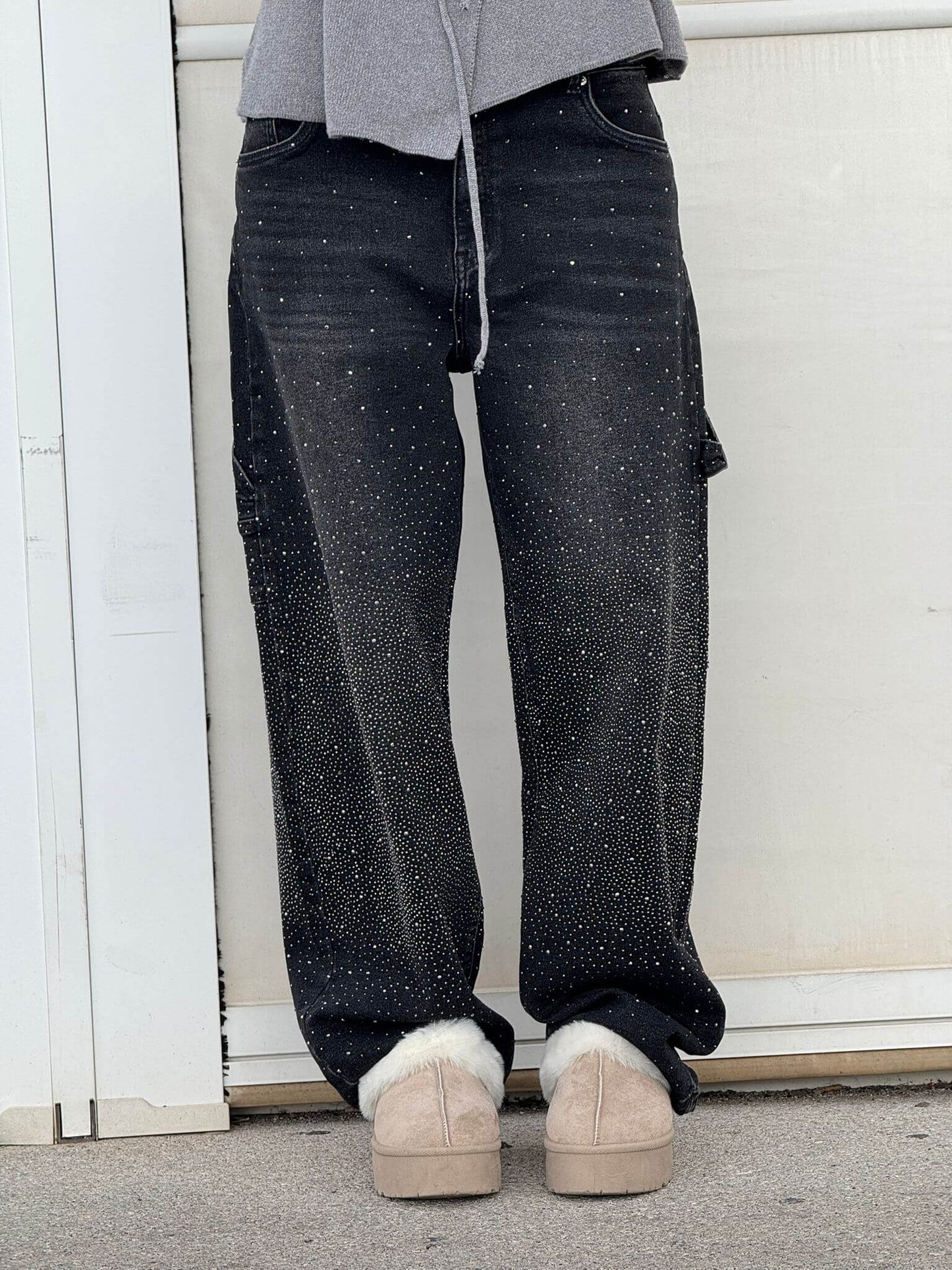 Jeans neri con dettagli scintillanti, indossati con scarpe beige invernali, su sfondo bianco. Moda casual, abbigliamento trendy, stile urbano.