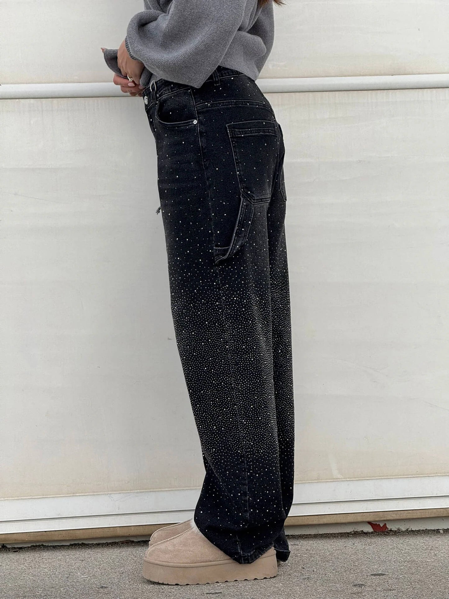 Jeans neri a vita alta con dettagli scintillanti, indossati da una persona di profilo. Scarpe beige con suola spessa. Moda casual elegante.