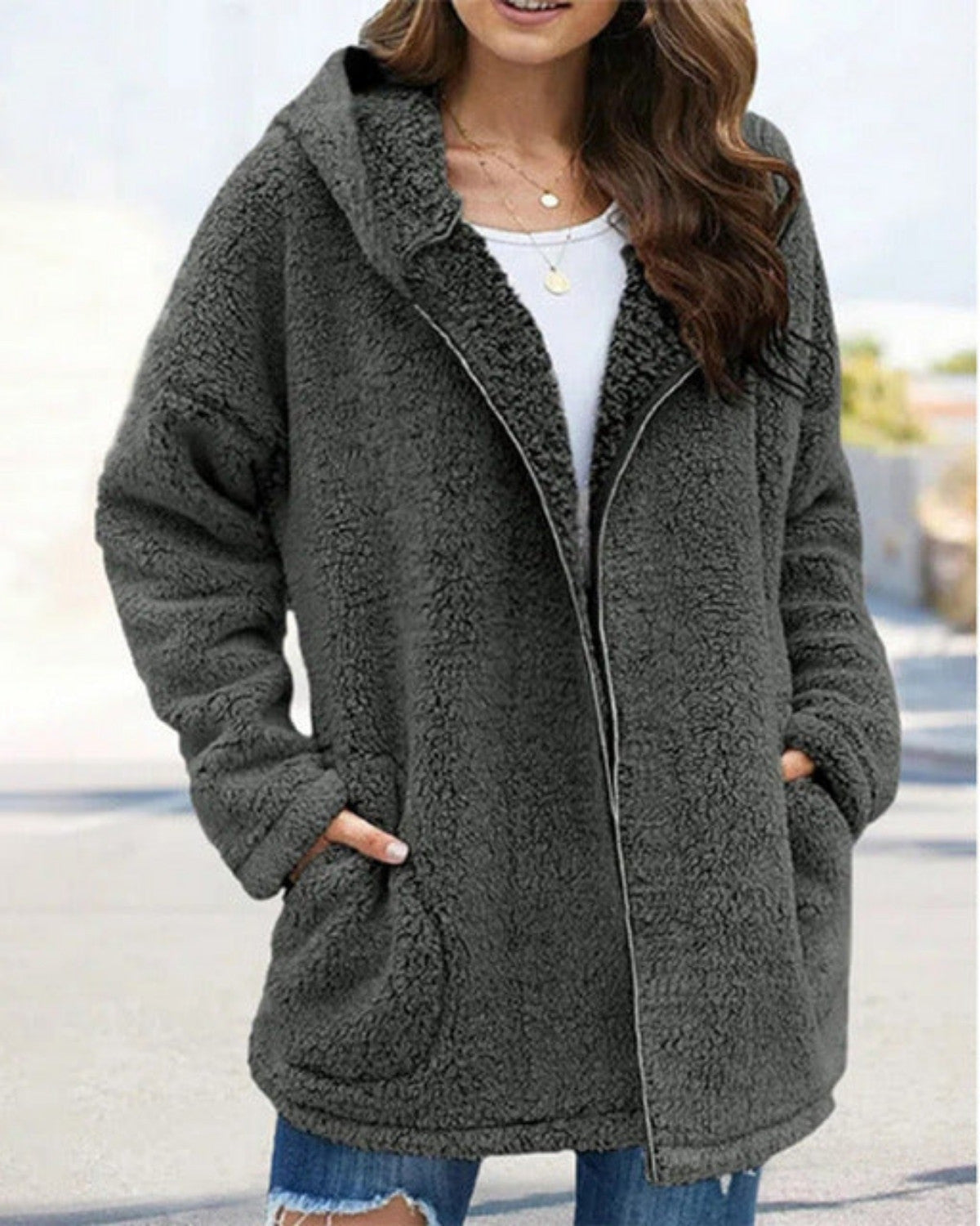 Donna con cappotto in pile grigio, cappuccio e tasche, indossa jeans strappati e maglietta bianca. Moda autunnale casual e confortevole.