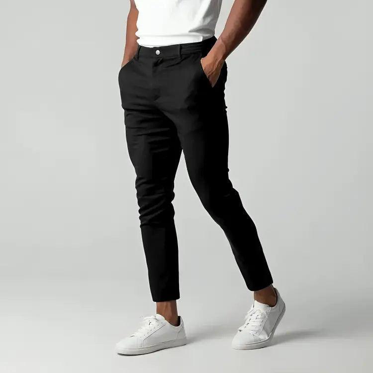 Pantaloni neri eleganti da uomo, abbinati a scarpe da ginnastica bianche e maglietta bianca, su sfondo grigio. Moda maschile casual chic.