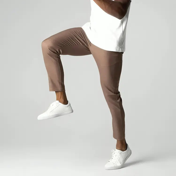 Uomo in pantaloni marroni e scarpe bianche, posa dinamica su sfondo grigio. Moda maschile, abbigliamento casual elegante, comfort e stile.