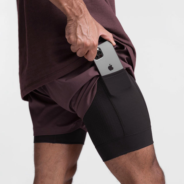 Uomo in pantaloncini sportivi neri con tasca laterale, inserisce smartphone. Abbigliamento fitness, tecnologia, comodità, design funzionale.