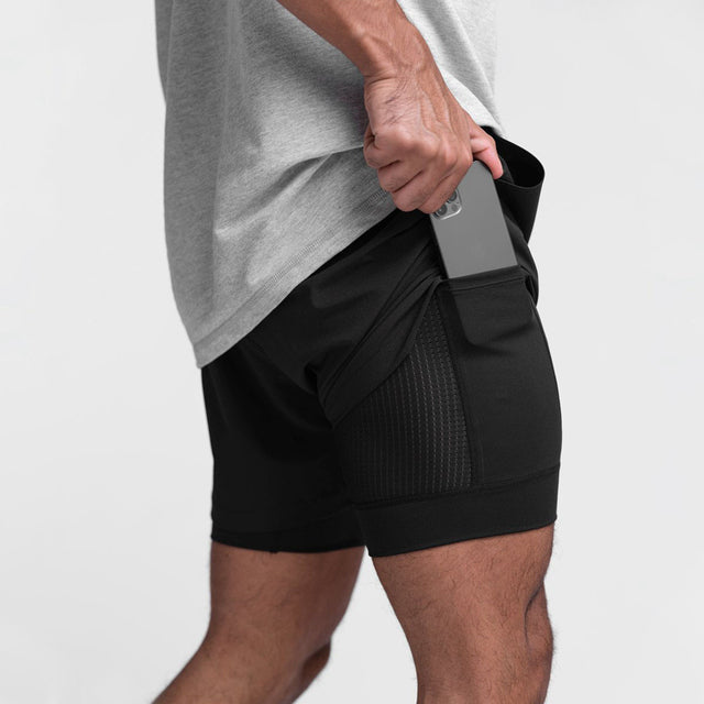Uomo in pantaloncini sportivi neri con tasca laterale, inserisce smartphone. Abbigliamento fitness, moda uomo, comodità, tecnologia portatile.