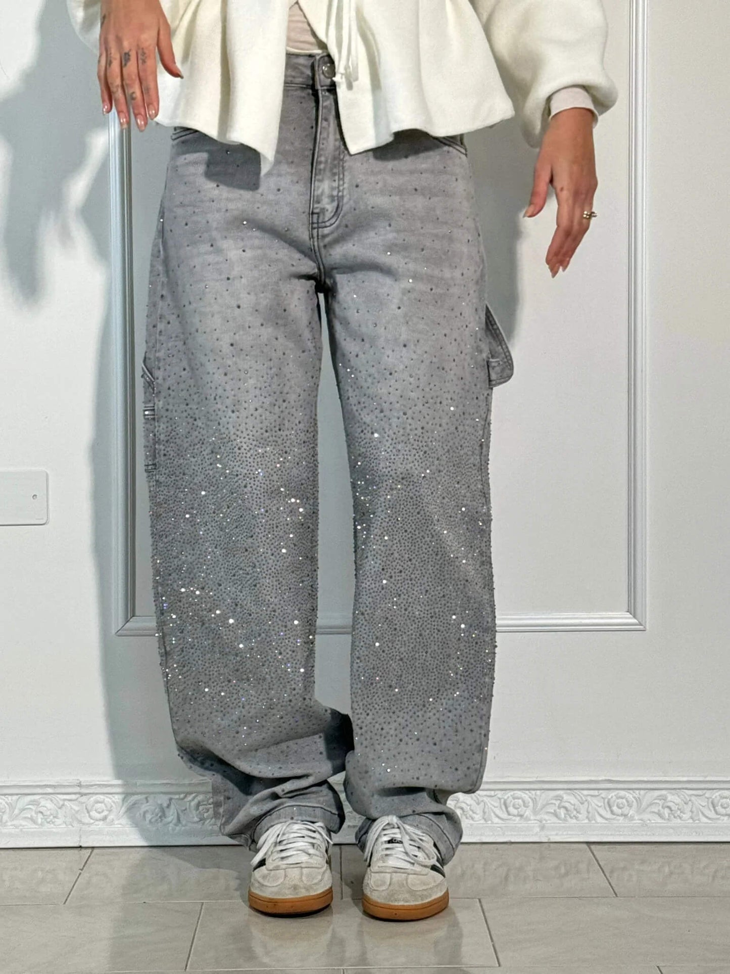 Jeans grigi larghi con strass scintillanti, abbinati a scarpe da ginnastica bianche. Moda casual, stile urbano, tendenza 2023.