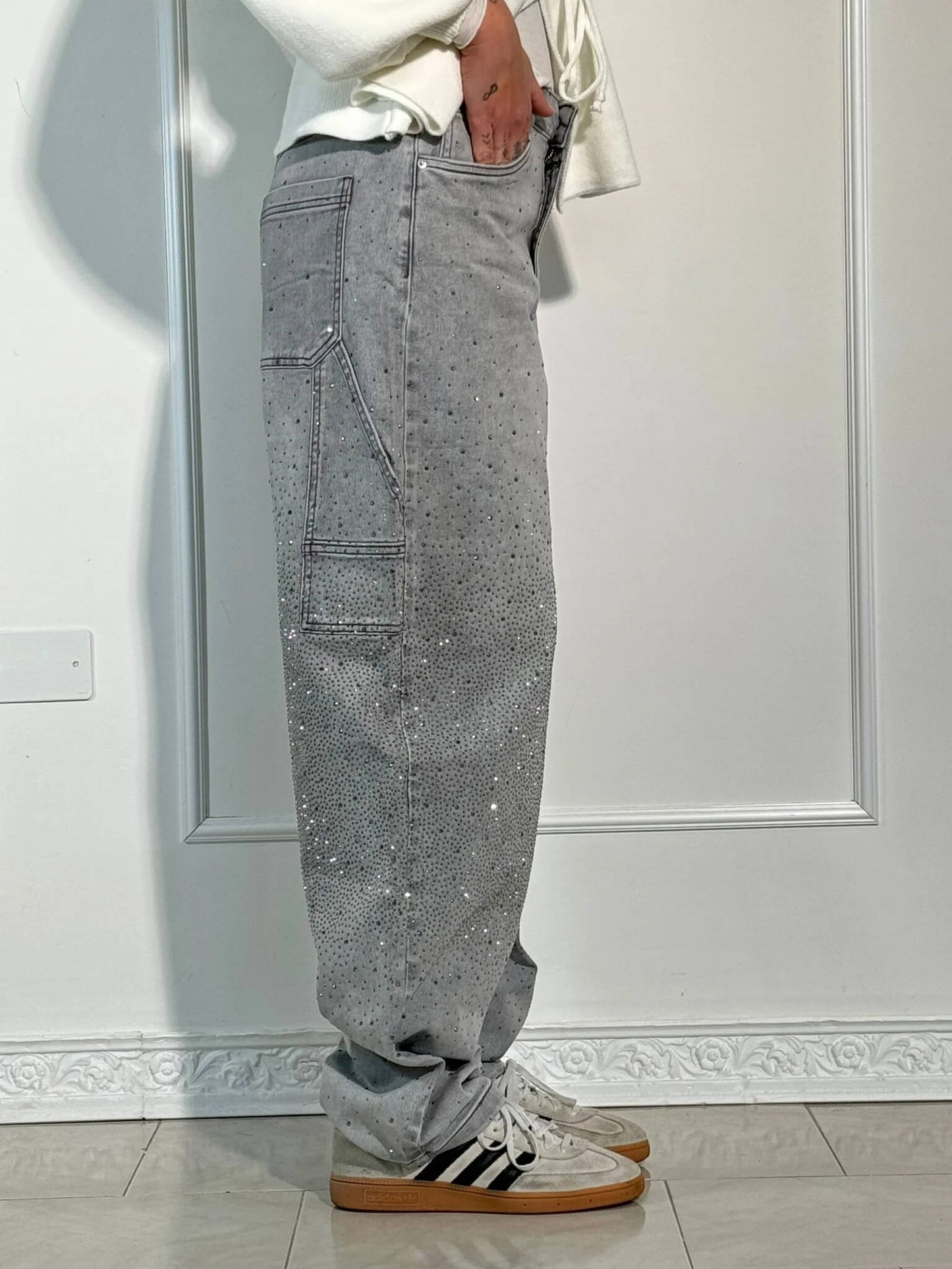 Pantaloni grigi con strass, tasche laterali, indossati con sneakers bianche e nere. Stile casual, moda uomo, abbigliamento trendy.