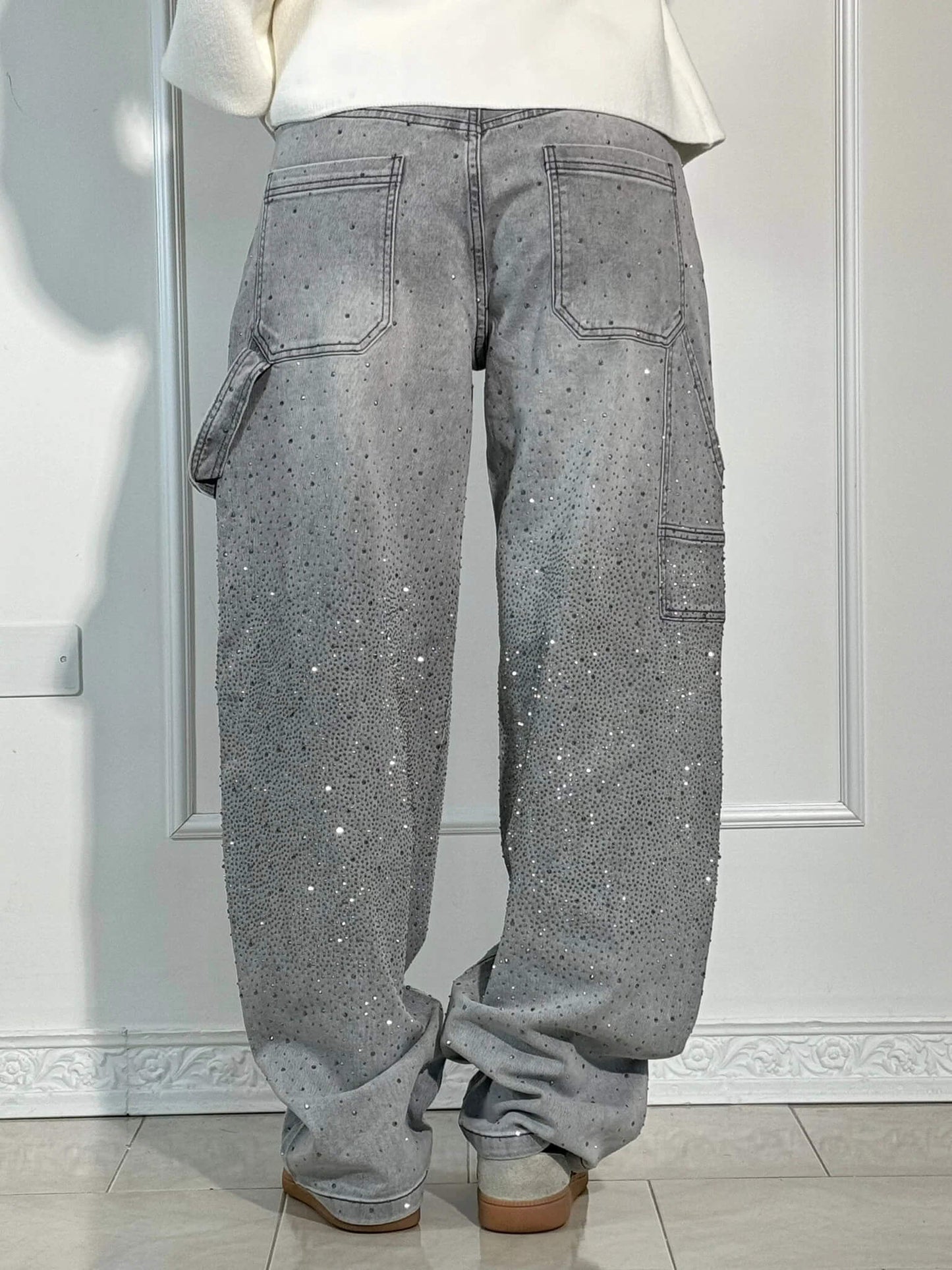 Jeans grigi con strass, tasche posteriori e laterali, indossati da una persona. Stile casual, moda streetwear, dettagli scintillanti.