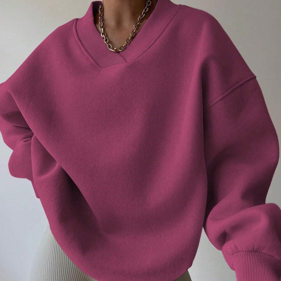 Maglione oversize fucsia con scollo a V, indossato con collana a catena dorata. Moda casual donna, tendenze abbigliamento autunno inverno.