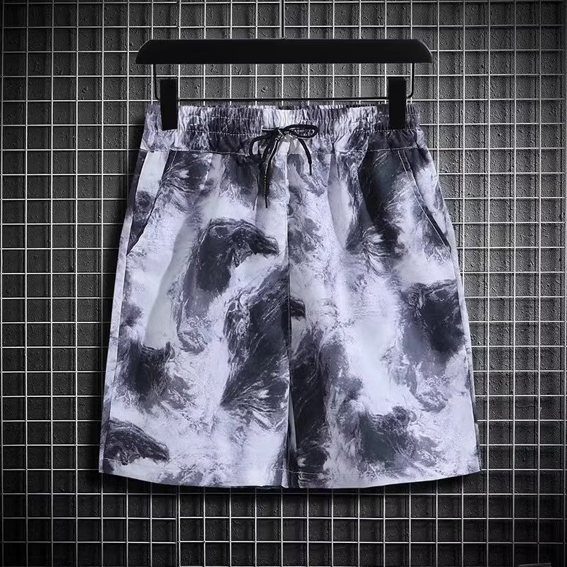 Pantaloncini sportivi uomo con stampa astratta bianco e nero, elastico in vita, tasche laterali, appesi su griglia metallica. Moda casual estiva.