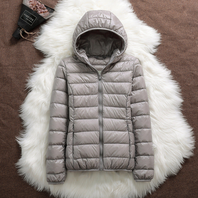 Giacca invernale imbottita grigia con cappuccio, su sfondo di pelliccia bianca. Moda donna, abbigliamento caldo, stile casual.