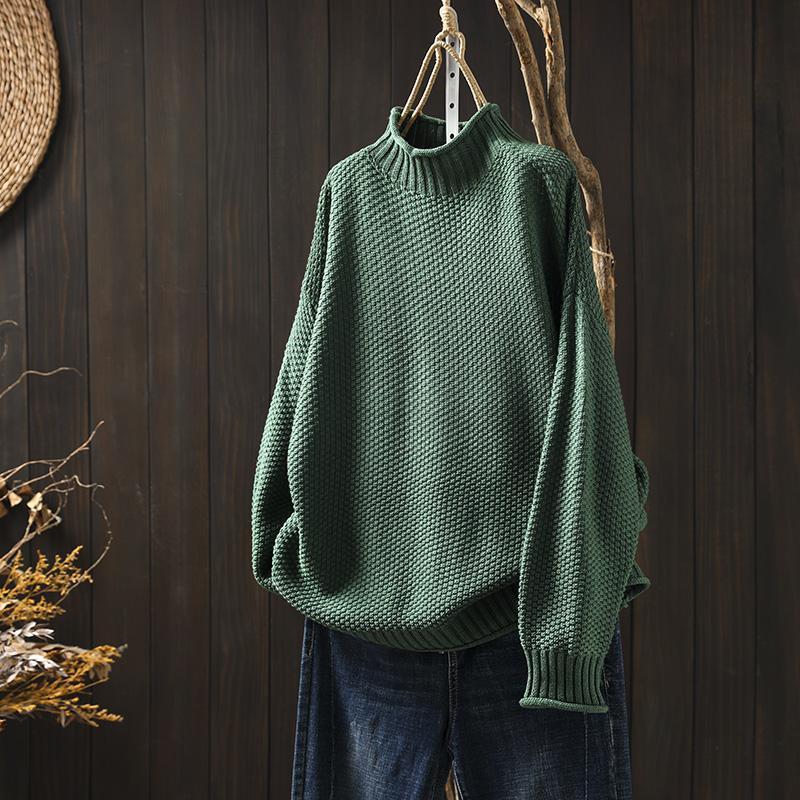 Maglione verde a collo alto in maglia spessa, appeso su sfondo di legno scuro, abbinato a jeans. Moda autunnale, abbigliamento casual elegante.