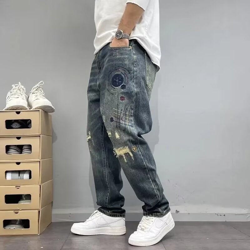 Jeans uomo strappati con dettagli ricamati, abbinati a scarpe da ginnastica bianche. Moda casual maschile, stile urbano moderno.