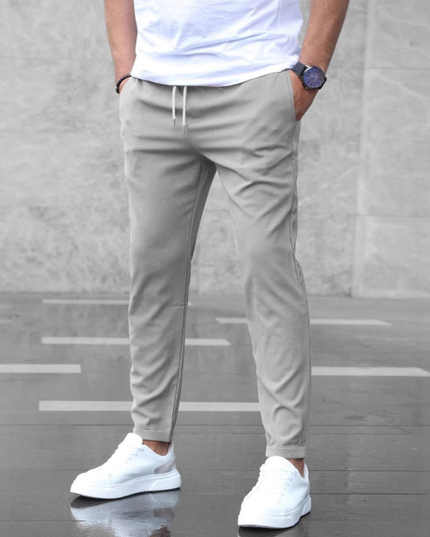 Uomo in pantaloni jogger grigi e scarpe da ginnastica bianche su sfondo grigio. Moda casual maschile, abbigliamento sportivo elegante.