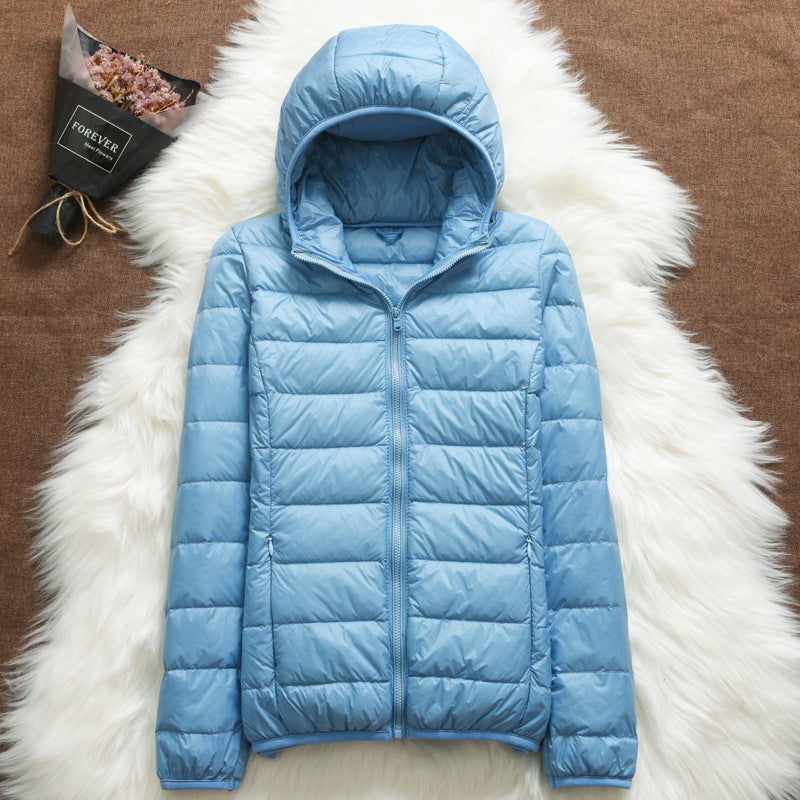 Giacca piumino azzurra con cappuccio su sfondo di pelliccia bianca, accanto a bouquet di fiori secchi. Moda invernale, abbigliamento caldo e leggero.