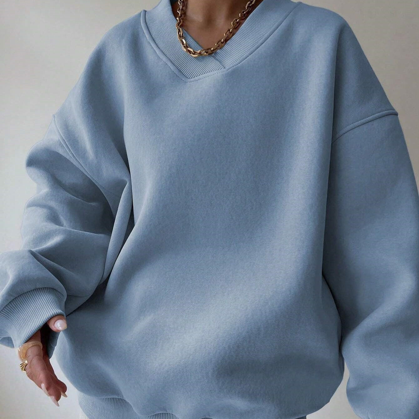 Felpa oversize blu chiaro, stile casual, indossata da una persona con collana dorata. Moda streetwear, abbigliamento comodo e trendy.