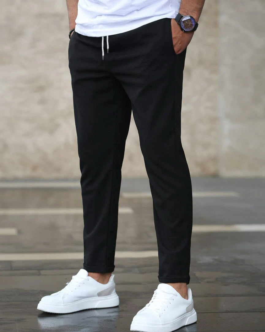 Uomo con pantaloni neri casual e scarpe da ginnastica bianche, sfondo urbano. Moda maschile, abbigliamento casual, stile moderno.