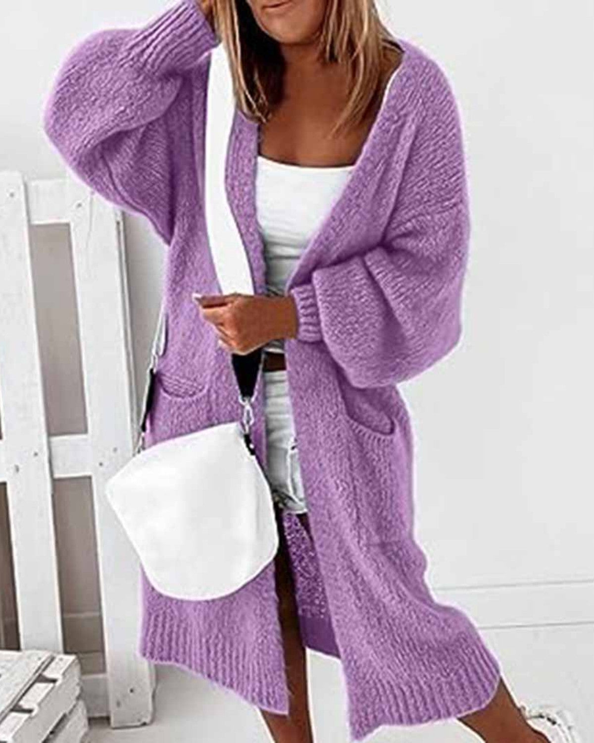Donna con cardigan lungo viola, abito bianco e borsa a tracolla bianca. Moda autunnale, abbigliamento casual elegante, stile femminile moderno.