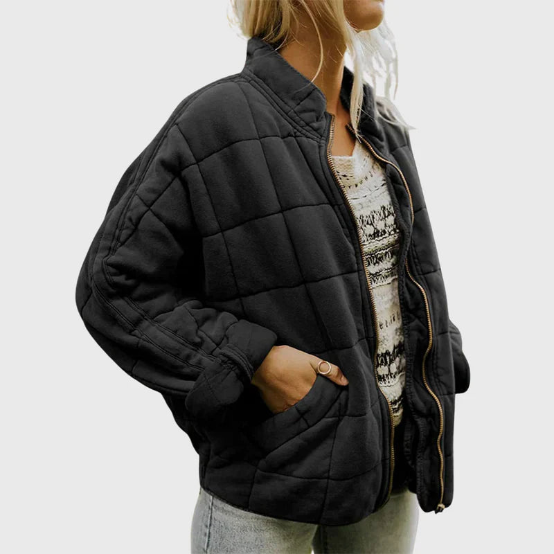 Giacca trapuntata nera da donna, stile casual, con zip aperta e mani in tasca, indossata su maglia bianca decorata, moda autunnale.