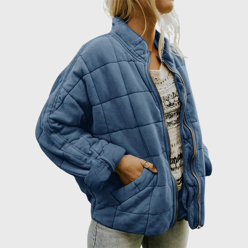 Donna con giacca trapuntata blu, zip aperta, indossa maglia bianca e jeans. Moda autunnale, abbigliamento casual, stile moderno.