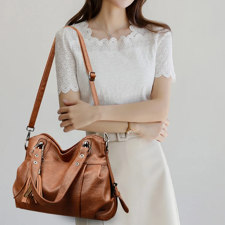 Donna con borsa a tracolla in pelle marrone, indossa una maglia bianca elegante e una gonna chiara. Moda femminile, accessori di tendenza.